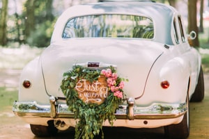 Ein alter Oldtimer, weißer Hochzeitswagen mit Blumen in Herzformen an der Stoßstange. Zwischen den Blumen ist ein Schild mit dem Satz Just Married.